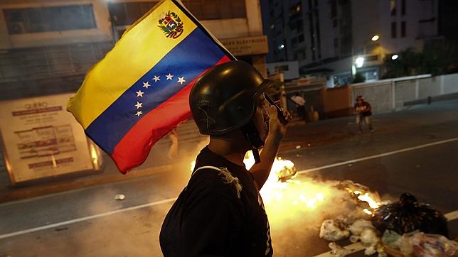 An opposition demonstrator carries a Venezuelan flag as he walks past a burning barricade during a protest in Caracas